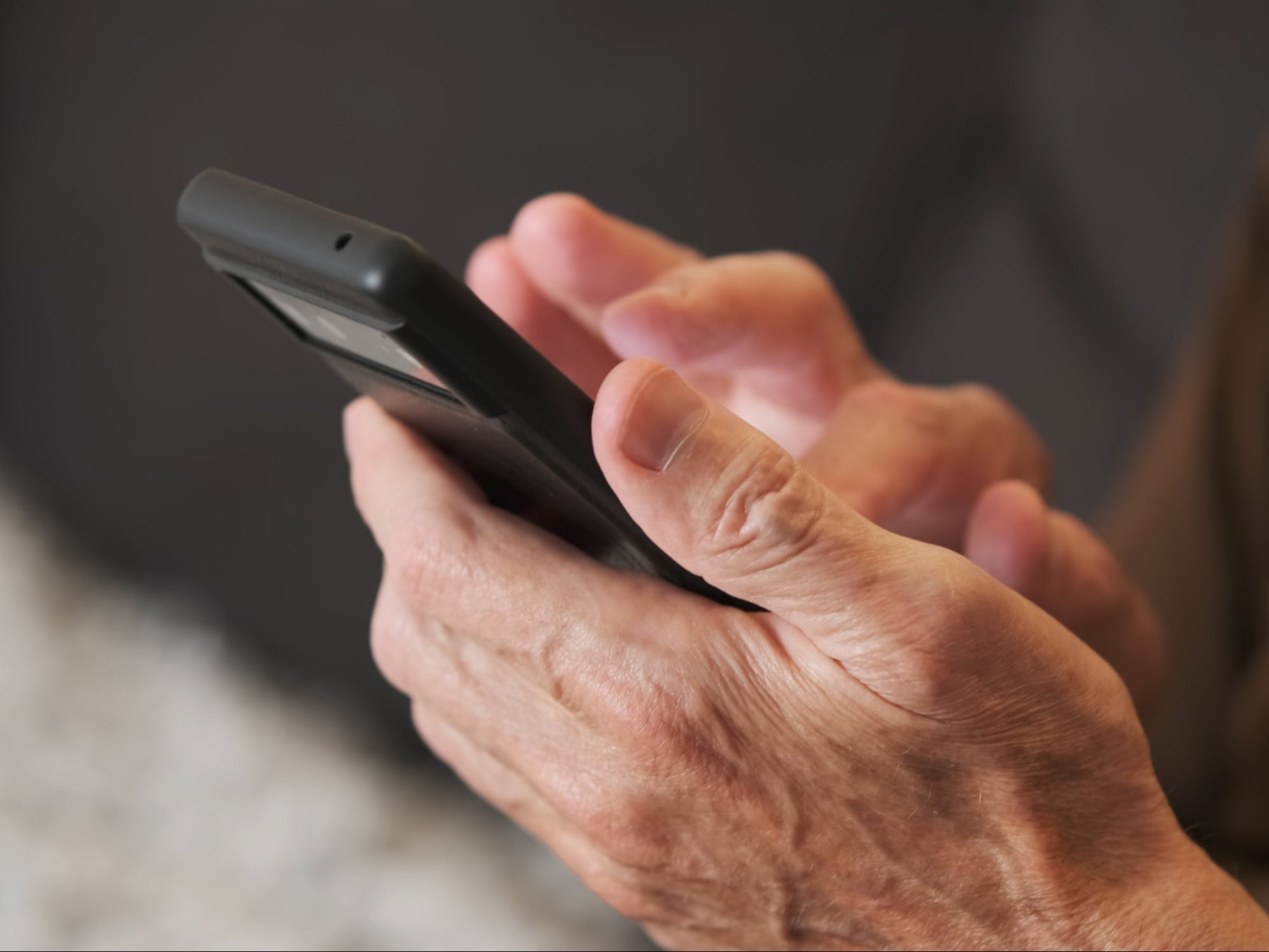 Close-up of a person's hands holding and using a black smartphone, with fingers actively typing or swiping on the screen.